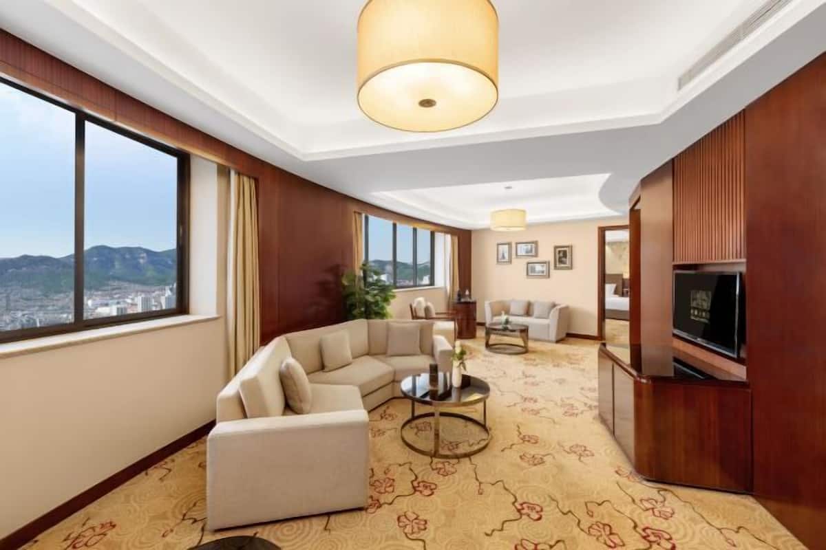 Ein Hotelzimmer mit großem Fenster und Blick auf die Stadt, einer Couch, einem Couchtisch und einem Fernseher.