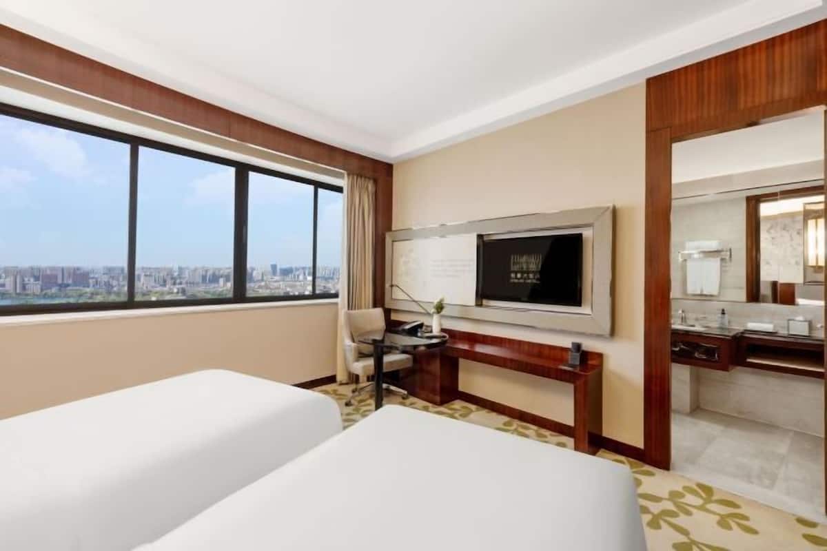 Ein Hotelzimmer mit zwei Betten, einem Fernseher, einem Schreibtisch und einem Badezimmer.