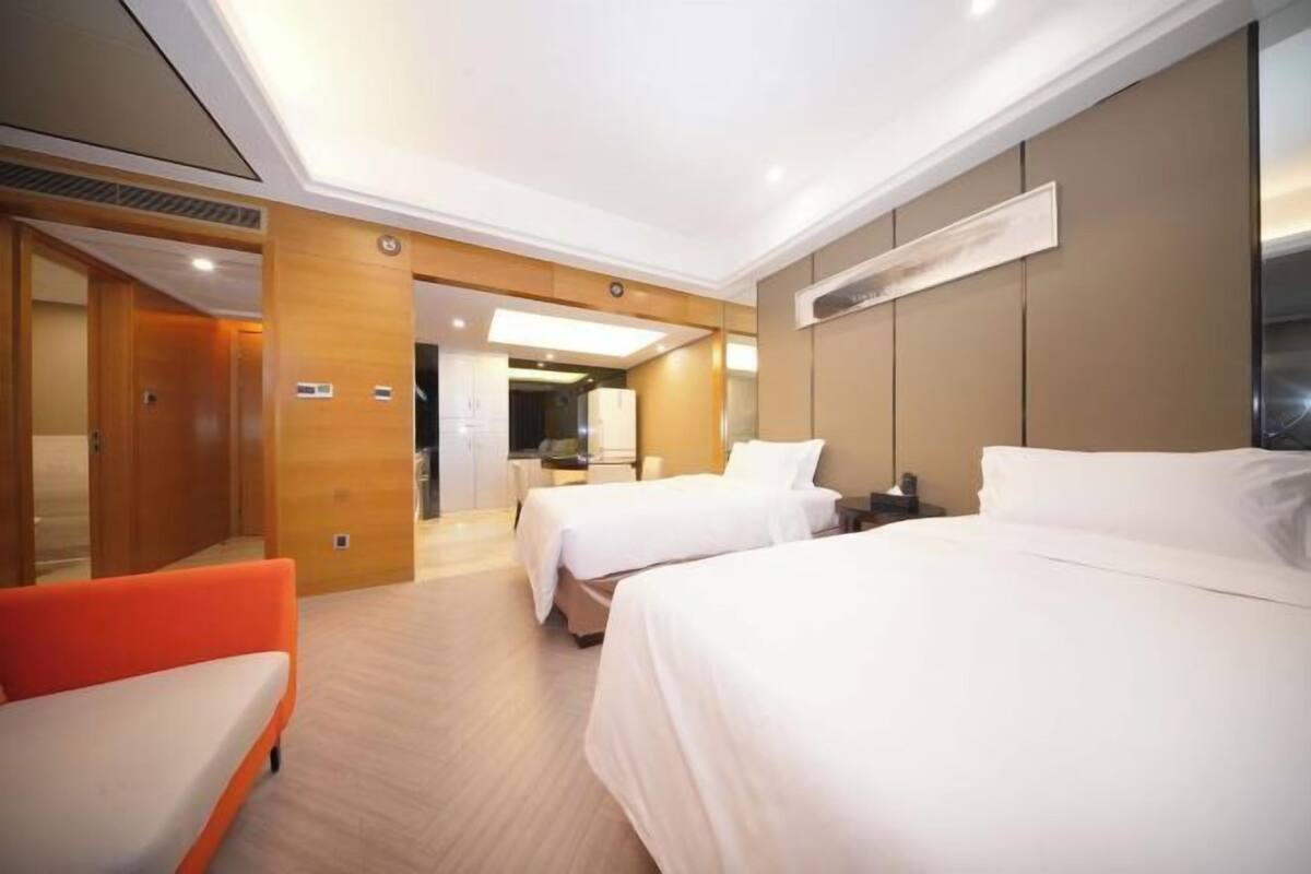Ein Hotelzimmer mit zwei Betten, einem Sofa, einem Schreibtisch und einem im Hintergrund sichtbaren Badezimmer.