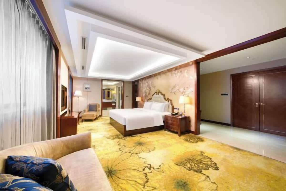 Ein Hotelzimmer mit einem Bett, einem Nachttisch, einer Lampe, einem Sofa und einem großen Teppich mit floralem Muster.
