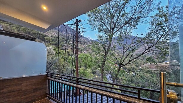 A balcony with a wooden floor and metal railing, overlooking a mountainous landscape with trees and a clear sky. - Aghor Guest House (Dharamshala)