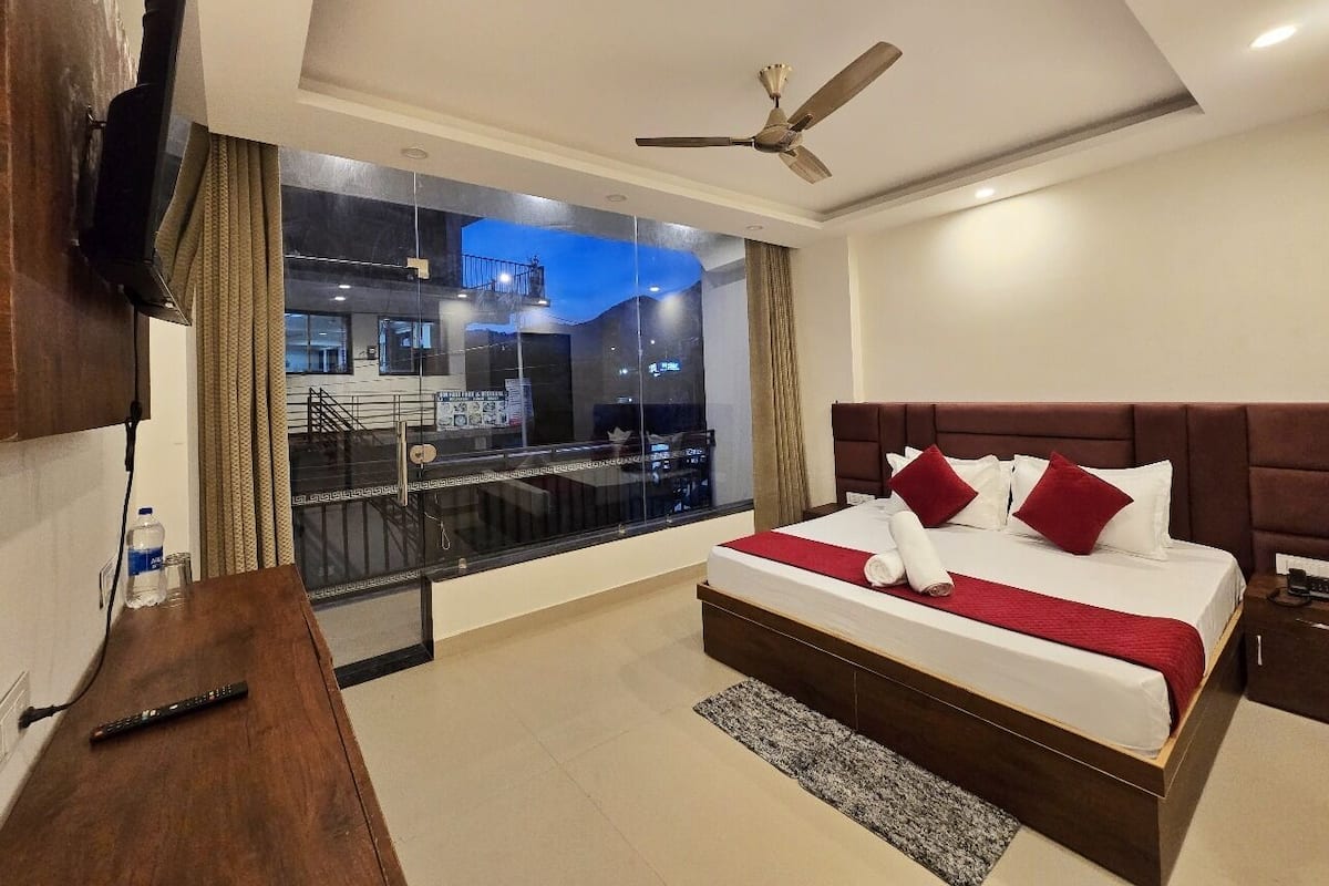 Quarto de hotel moderno com uma cama grande, ventoinha no teto, televisão na parede e varanda com vista para a cidade.