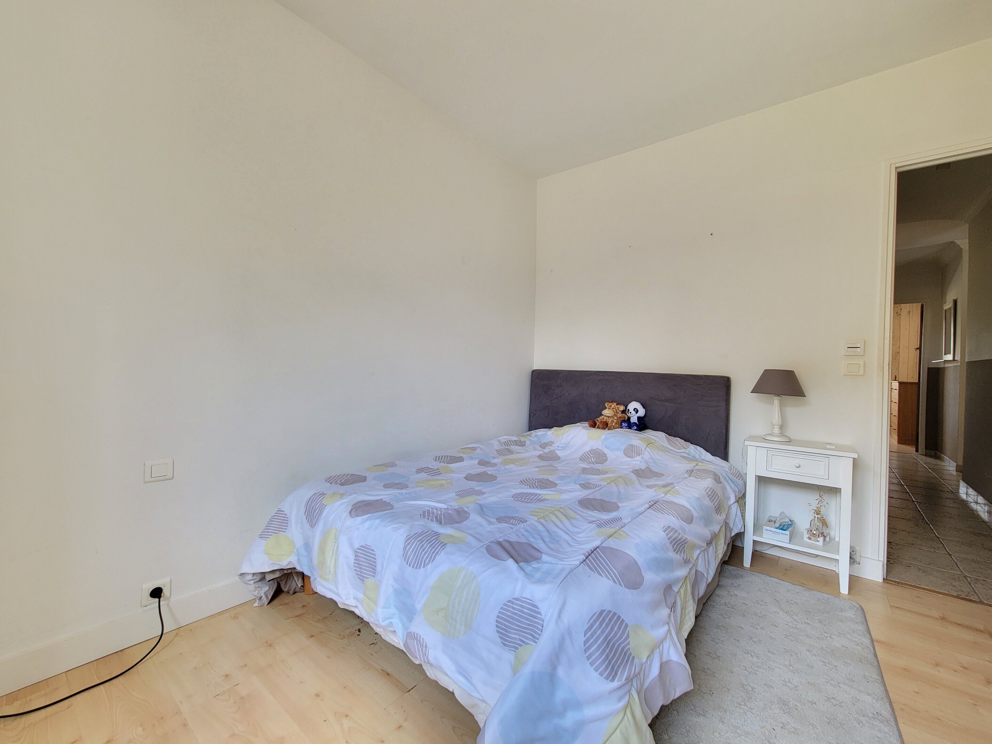 A bedroom with a bed, a nightstand, a lamp, and a door leading to another room.