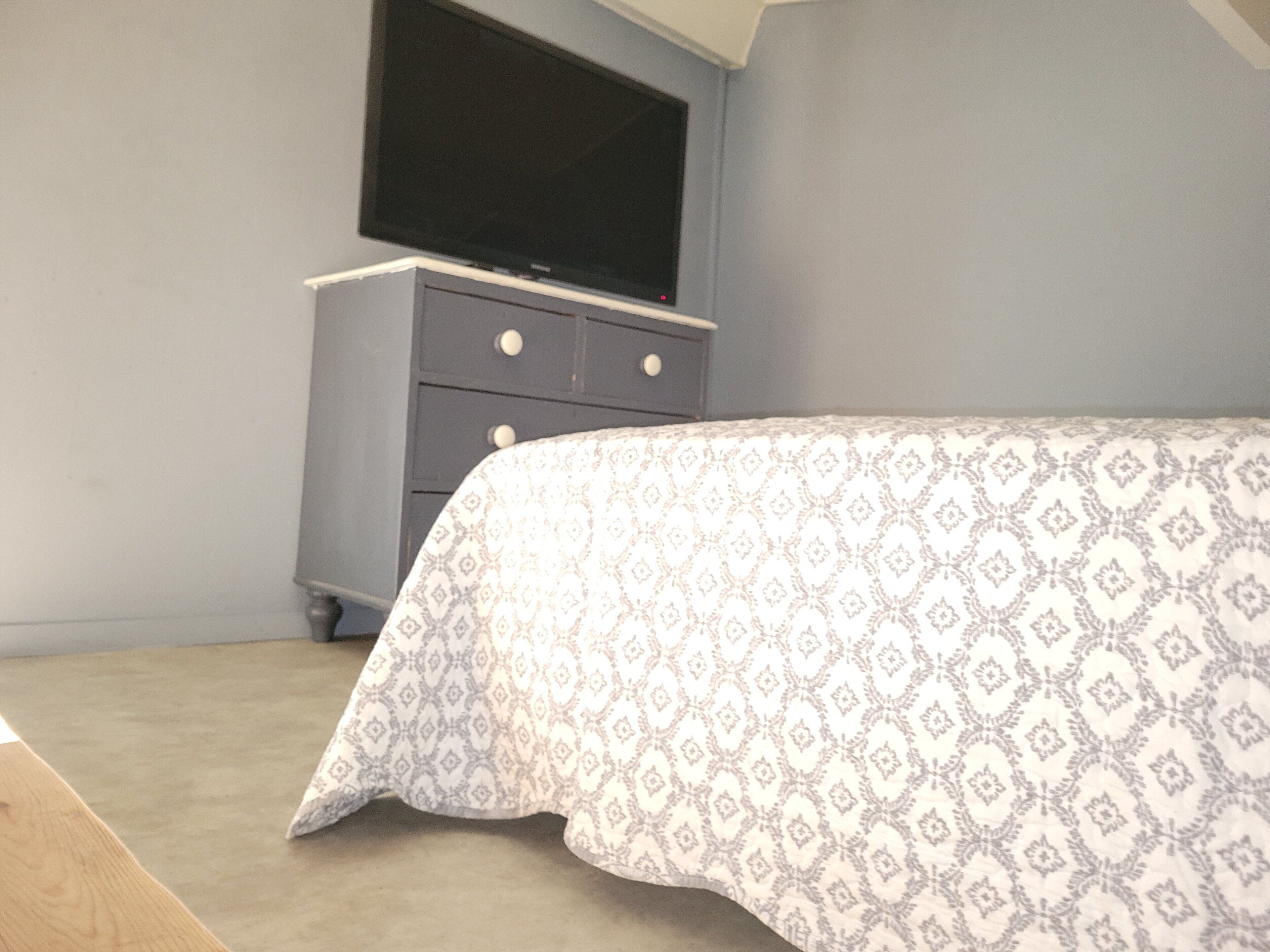 Une chambre à coucher avec un lit, une commode et un téléviseur fixé au mur.