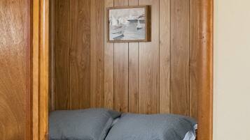 A bedroom with a wooden paneled wall, a bed with grey bedding, and a framed picture above the bed.