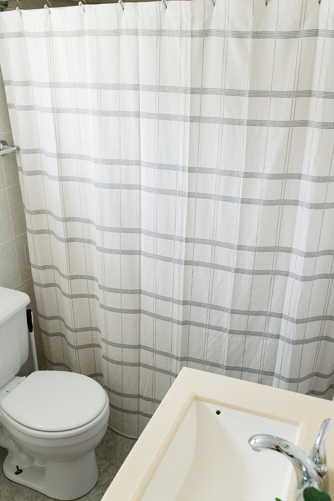 A bathroom with a white toilet, a sink with a chrome faucet, and a shower curtain with a plaid pattern.