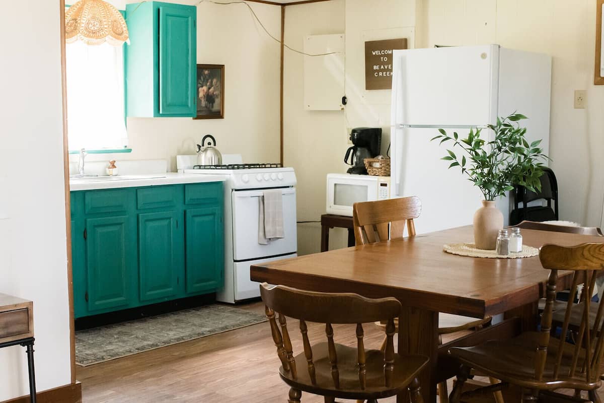 Een keuken met turquoise kastjes, een witte kookplaat en een eettafel met houten stoelen.
