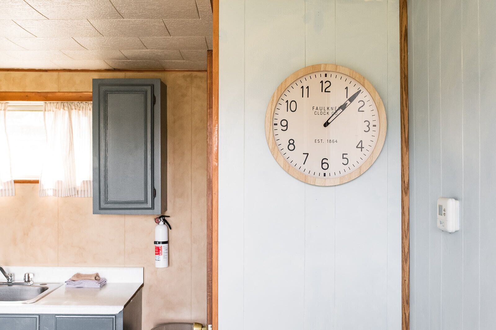 A kitchen with a wooden cabinet, a sink, and a wall-mounted clock.