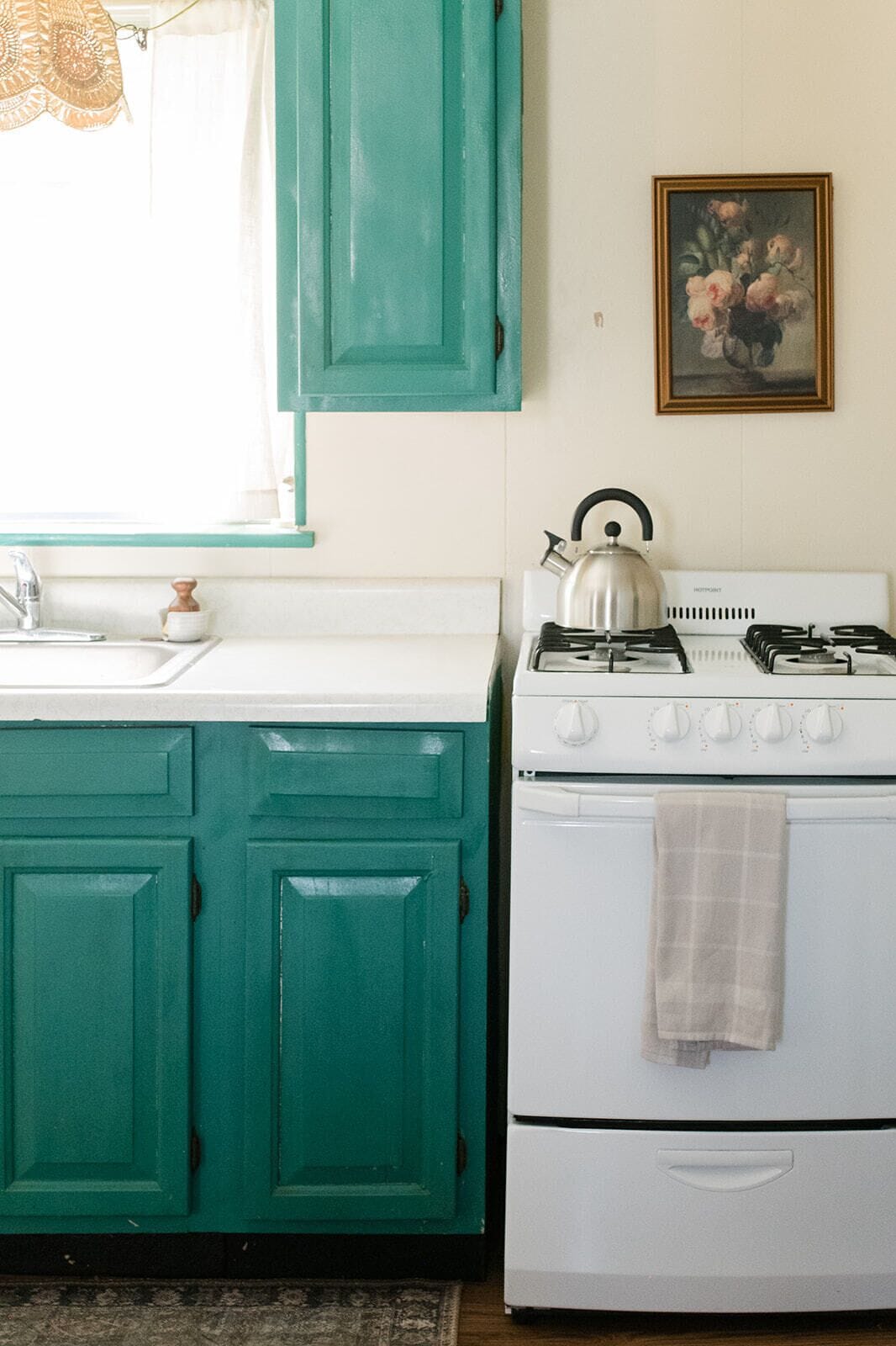 A kitchen with teal cabinets, a white stove, and a painting on the wall.
