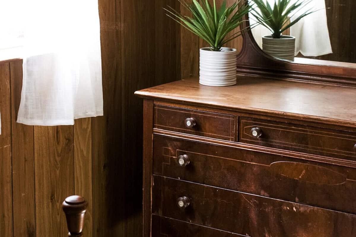 Een houten dressoir met lades, een spiegel en twee potplanten.