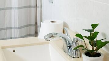A bathroom with a white sink, a mirror, a shower curtain, and a potted plant.
