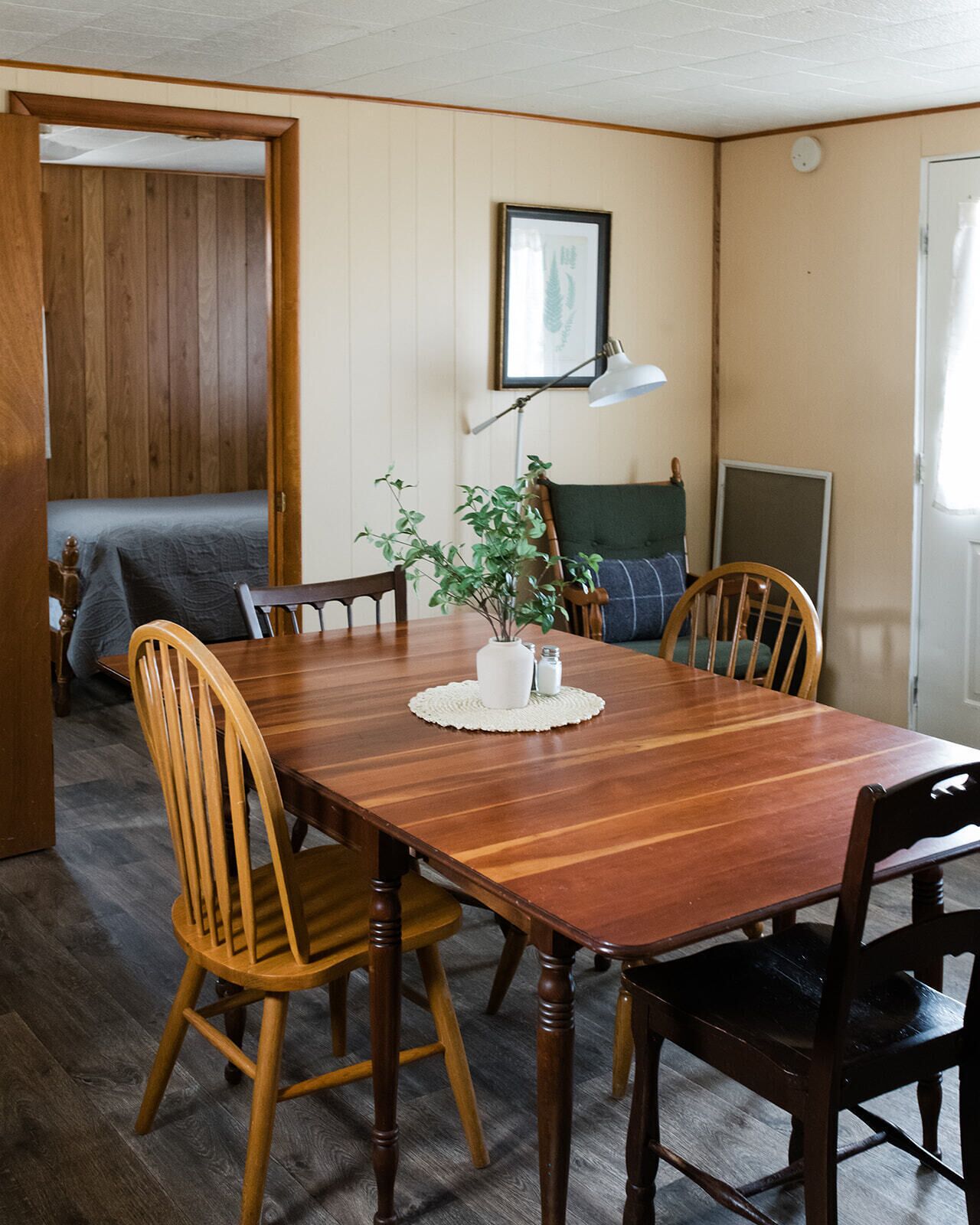 Une table à manger en bois, avec six chaises, une petite plante et un tableau encadré accroché au mur.