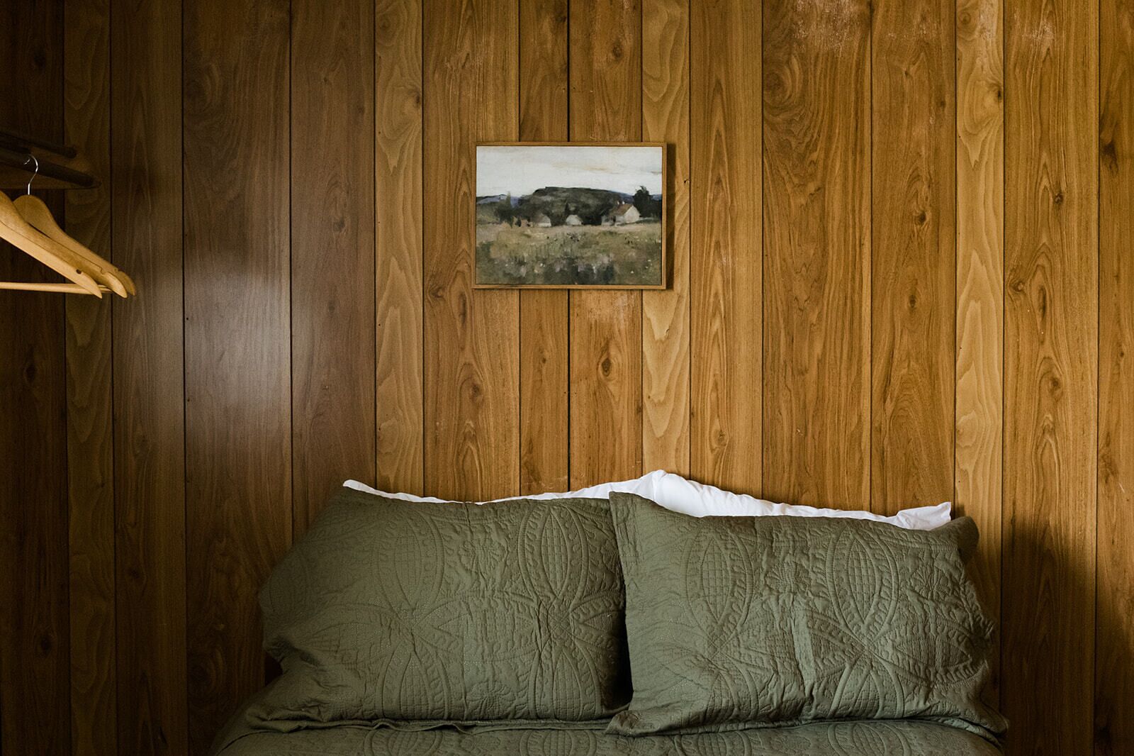 A room with wooden panel walls, a bed with green bedding, and a framed picture on the wall.