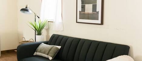 A dark green sofa with a single pillow, a small potted plant, a desk lamp, and a framed picture on the wall.