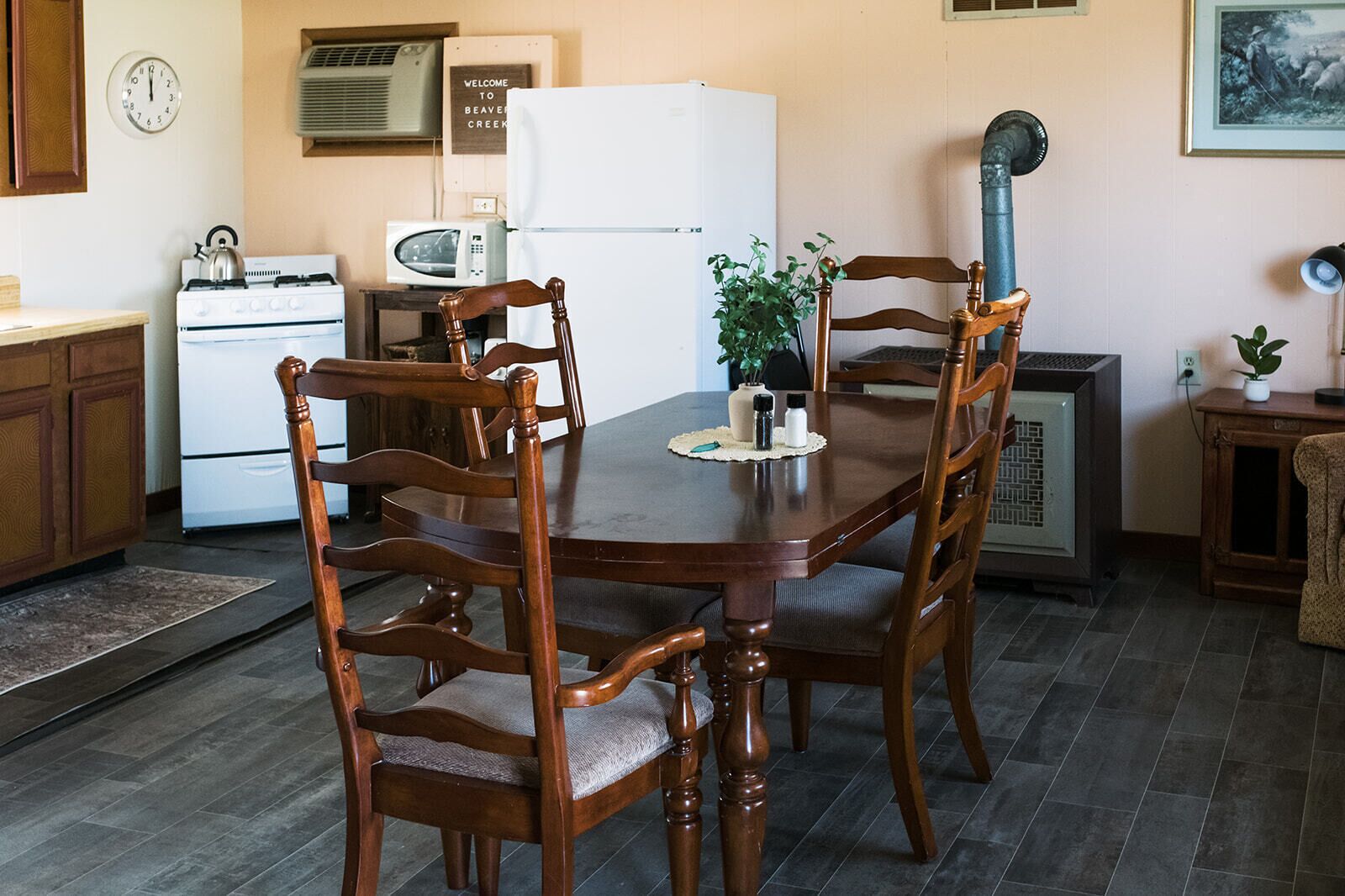 A dining area with a wooden table and chairs, a white refrigerator, a microwave, and a clock on the wall.
