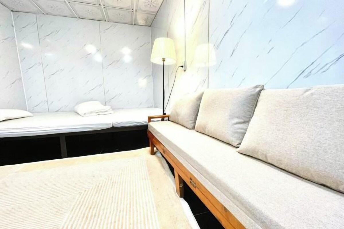A room with a bed, a sofa, a lamp, and a patterned rug.