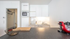 A modern kitchen with white cabinets, a black countertop, a microwave, a sink, and a red coffee machine. - Sunny Stay by the Seaside (Knokke-Heist)