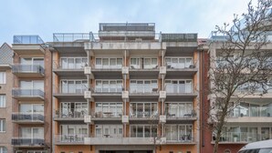 A multi-story residential building with balconies, a garage, and parked cars. - Sunny Stay by the Seaside (Knokke-Heist)
