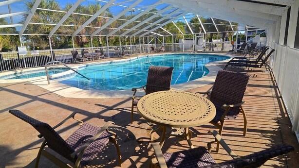 A covered pool area with lounge chairs and a table, surrounded by a white fence and palm trees. - Boat Slip - Pool- Screened balcony- Water front. 30 DAY MINIMUM STAY. (Gulf Shores)