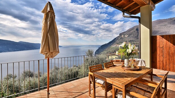 Une terrasse en bois avec une table et des chaises, offrant une vue sur un lac et des montagnes.