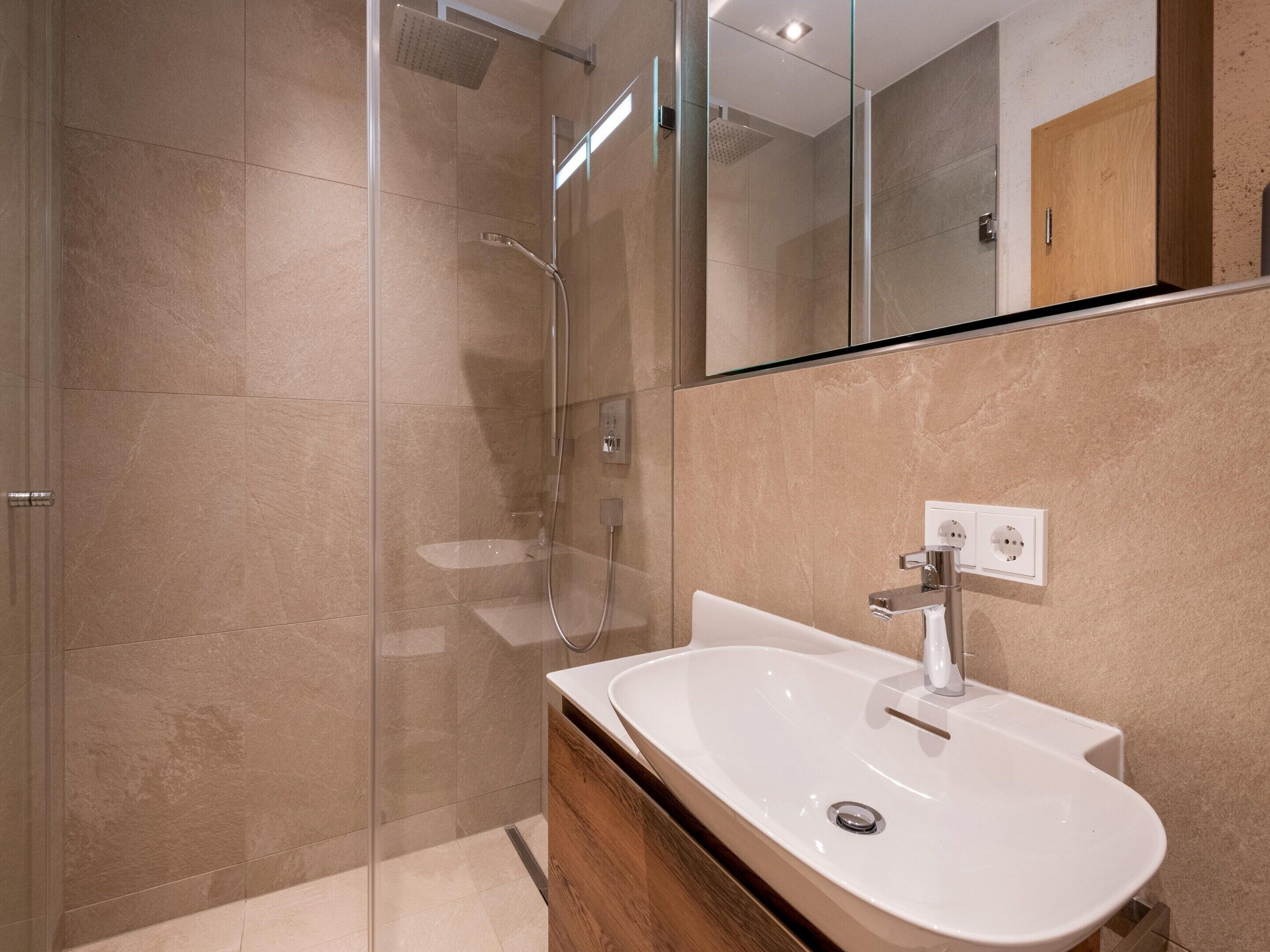 Ein modernes Badezimmer mit einer Duschkabine, einem weißen Waschbecken und einem Holz-Waschtisch.
