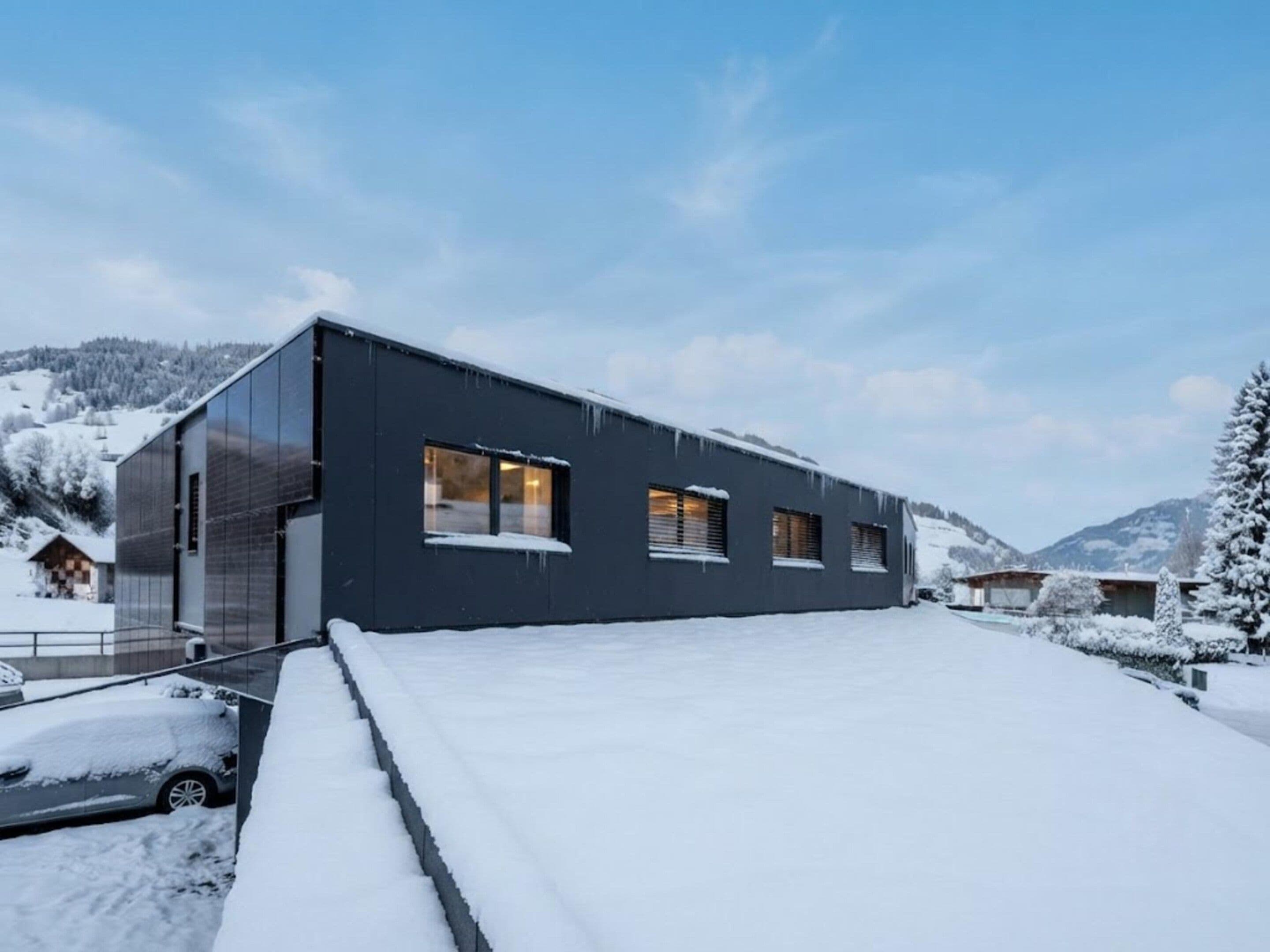 A modern building with large windows and a flat roof, surrounded by snow-covered landscape and mountains.