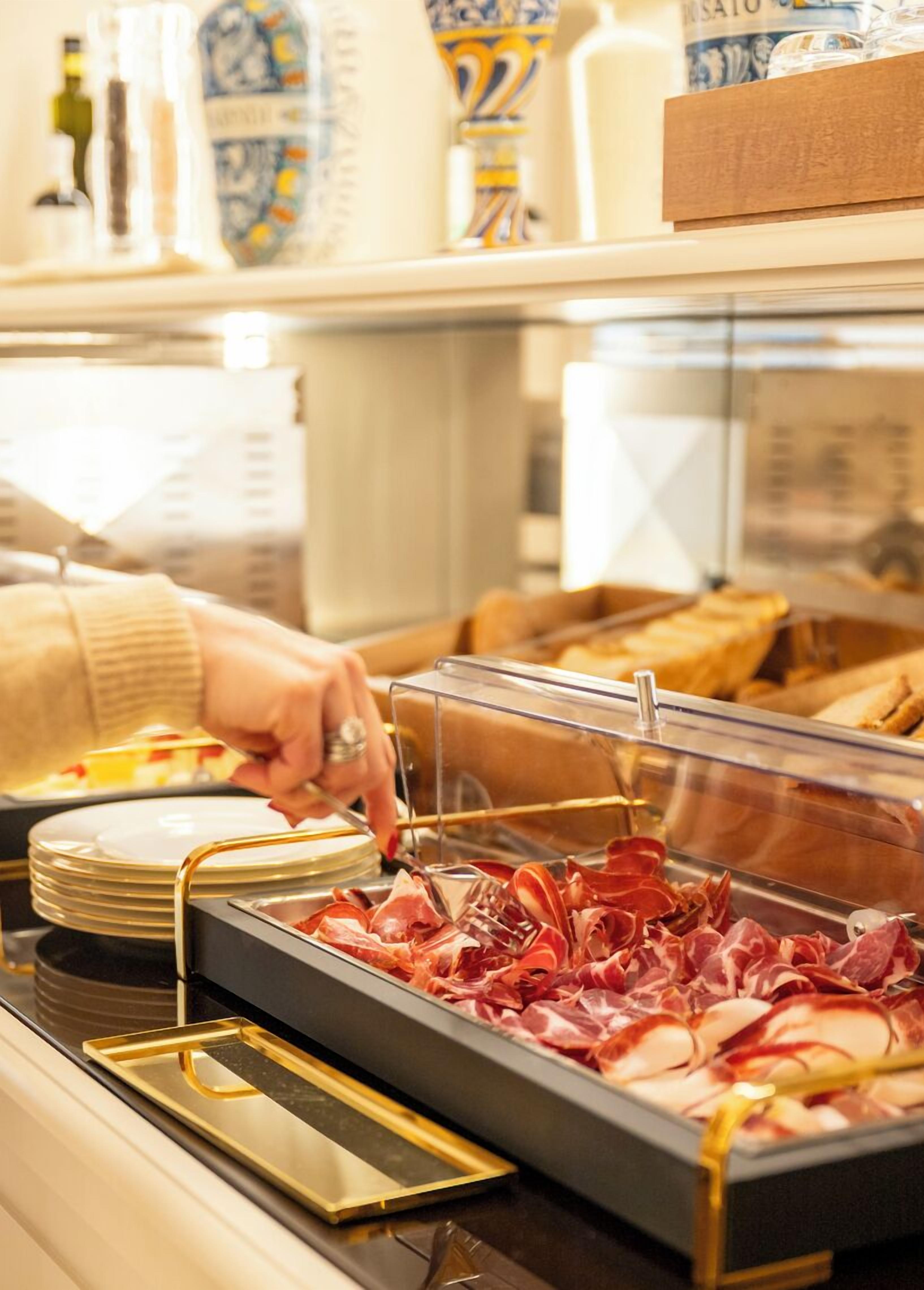 A buffet with a variety of meats and a person serving themselves.