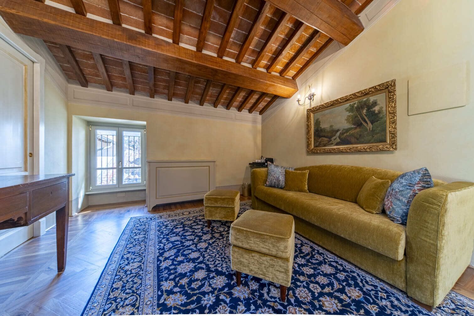 Un salon spacieux avec un plafond en bois, un grand canapé, un pouf assorti et un tapis à motifs.
