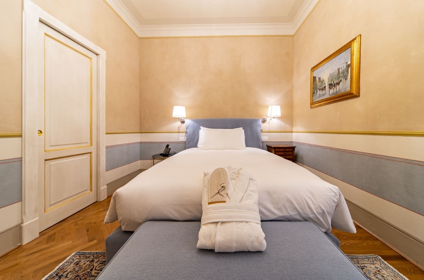 A hotel room with a large bed, bedside lamps, a framed picture on the wall, and a neatly folded robe on the bed.