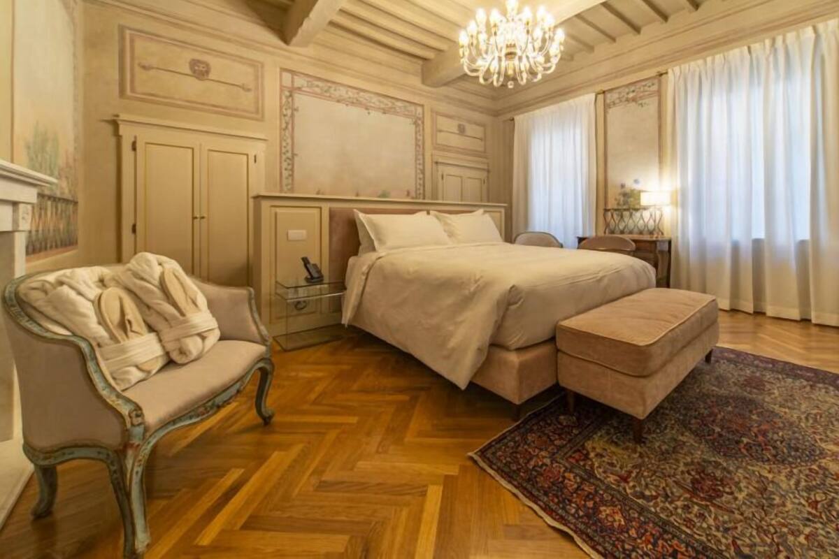 Un dormitorio con una cama grande, un chaise lounge, una mesita de noche y una araña.