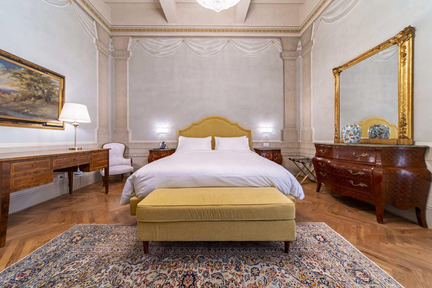 A spacious bedroom with a large bed, a wooden dresser, a desk, and a chair.