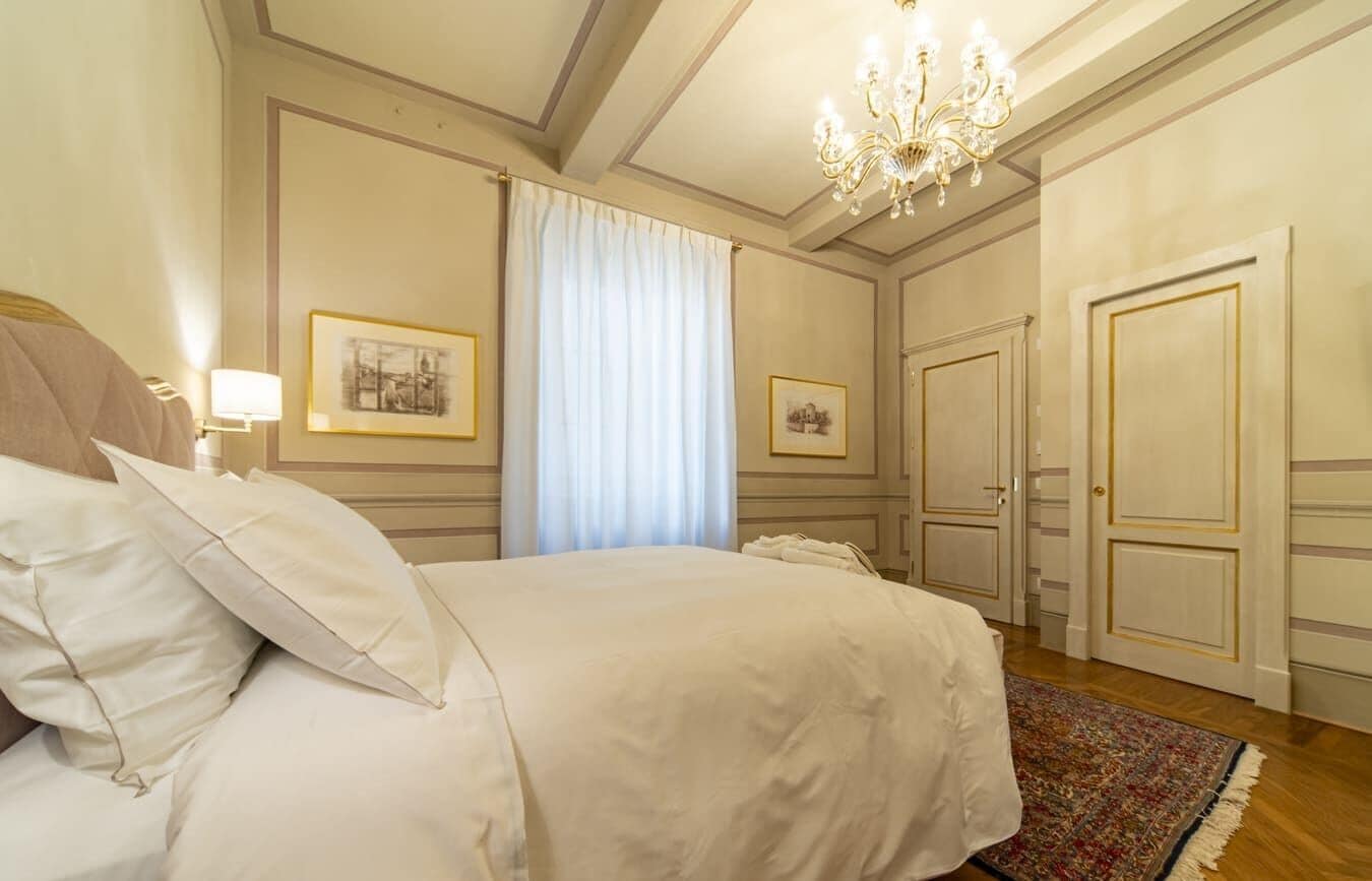 A hotel room with a large bed, a chandelier, framed pictures on the wall, and a door with a gold frame.