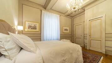 A hotel room with a large bed, a chandelier, framed pictures on the wall, and a door with a gold frame.