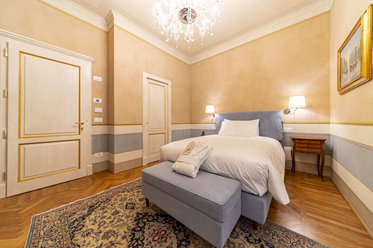 Un dormitorio con cama, mesita de noche, silla y candelabro.