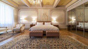 A spacious bedroom with a large bed, two side tables, a chaise lounge, and a large mirror.