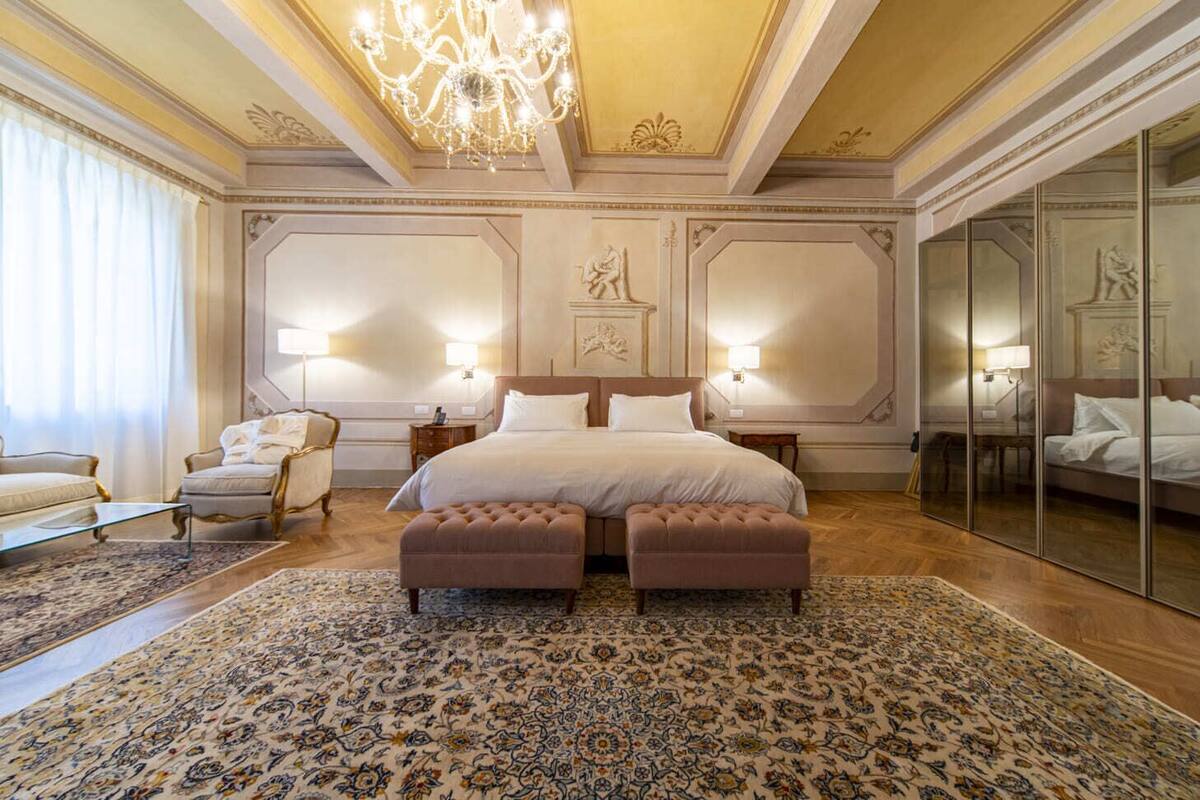 Un dormitorio amplio con una cama grande, dos mesitas de noche, un sillón y un espejo grande.