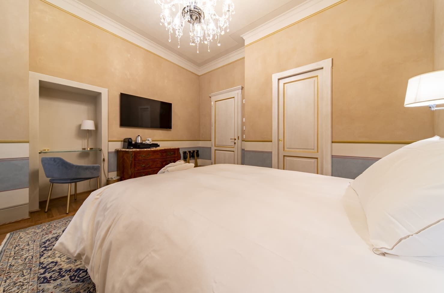 Camera d'albergo con un grande letto, una scrivania con sedia, una televisione e un lampadario.
