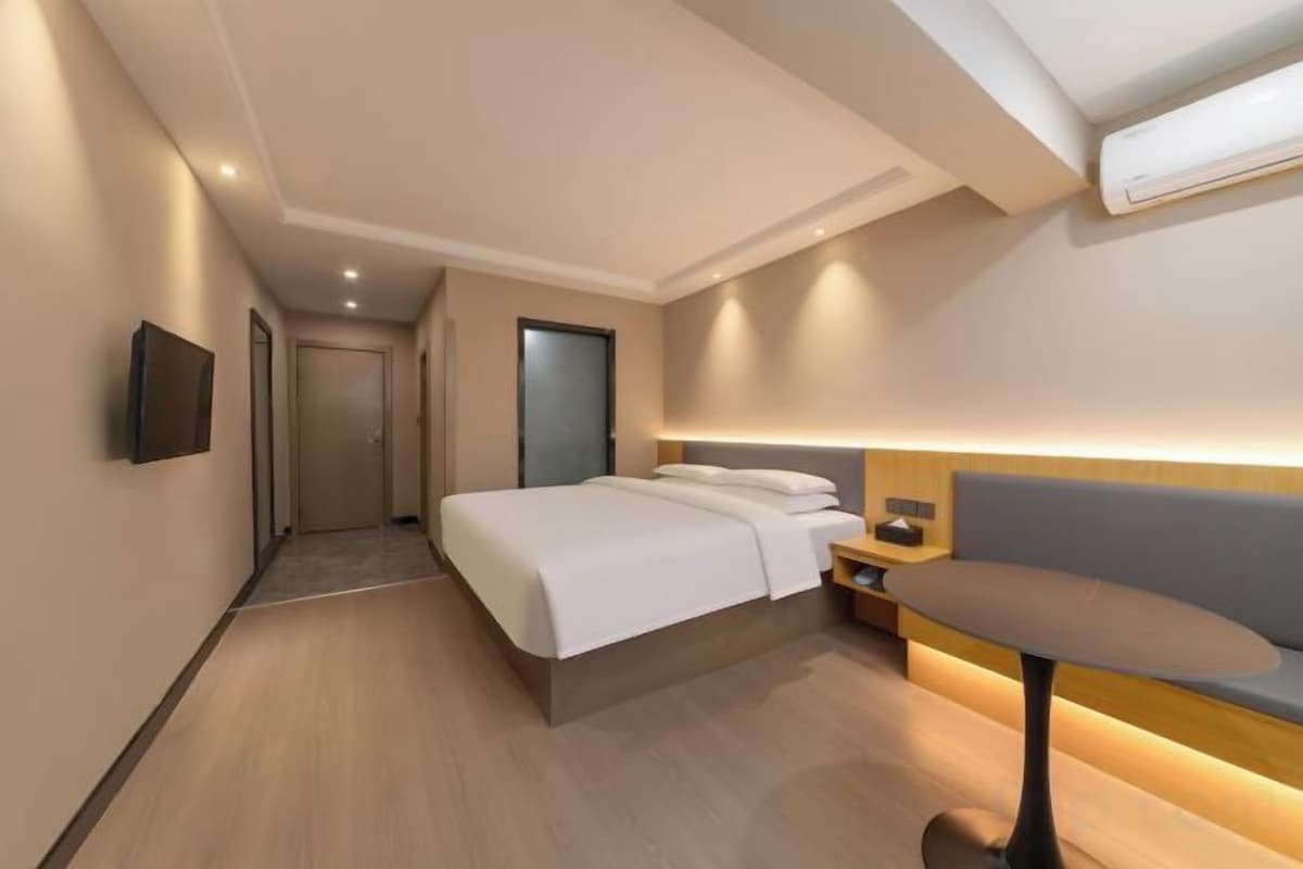 A modern hotel room with a bed, bedside table, and a small seating area.