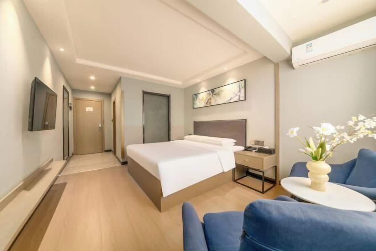 Een moderne hotelkamer met een groot bed, nachtkastje, stoel, klein tafeltje met een bloemenvaas en een aan de muur bevestigde televisie.