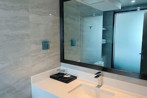 Ein modernes Badezimmer mit einem großen Spiegel, einem weißen Waschbecken und einer Duschkabine aus Glas.