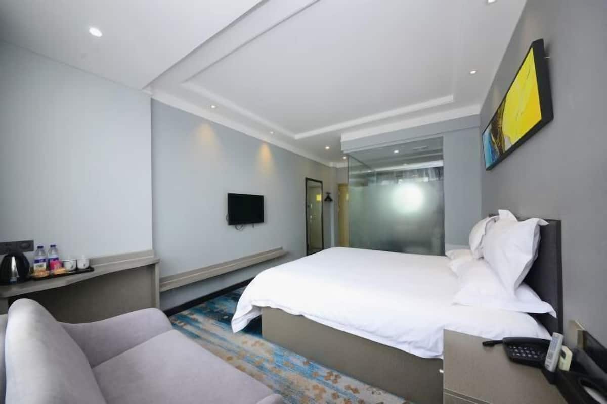 Hotelkamer met een bed, een bureau met telefoon, een stoel, een televisie en een badkamer zichtbaar door een glazen deur.