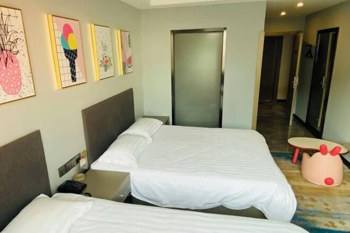 Een hotelkamer met twee bedden, een tafeltje en een deur naar een gang.