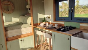 A cozy room with a bed, a small kitchen area with a stove, and a window with a view of greenery.