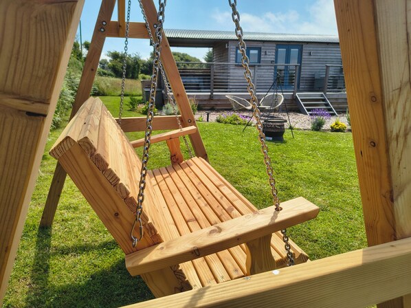 A wooden swing set with a bench seat, metal chains, and a metal frame. - Fir Tree Shepherd's Hut (Llanon)