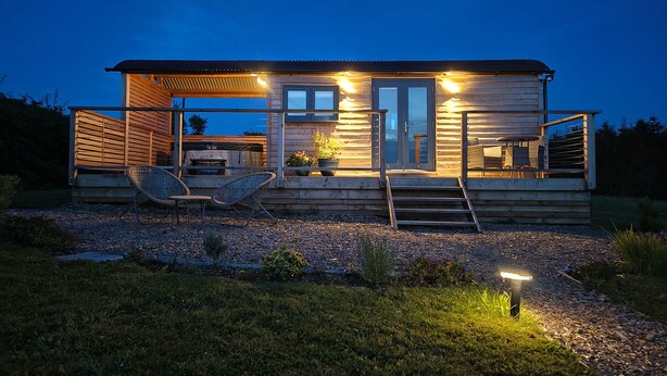 A wooden cabin with a deck, outdoor seating, and a grill area.