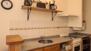 A kitchen with a granite countertop, stainless steel sink, wooden cabinets, a stove, and a coffee maker on a shelf. - Departamento en el centro para 4 pax (San Martín de los Andes)