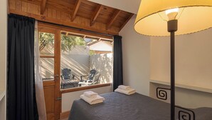 A bedroom with a bed, a window with curtains, a lamp, and a view of outdoor furniture. - Departamento en el centro para 4 pax (San Martín de los Andes)