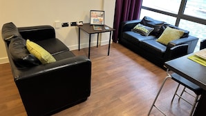 Una sala de estar moderna con dos sofás de cuero negro, una mesita y una ventana con cortinas moradas.