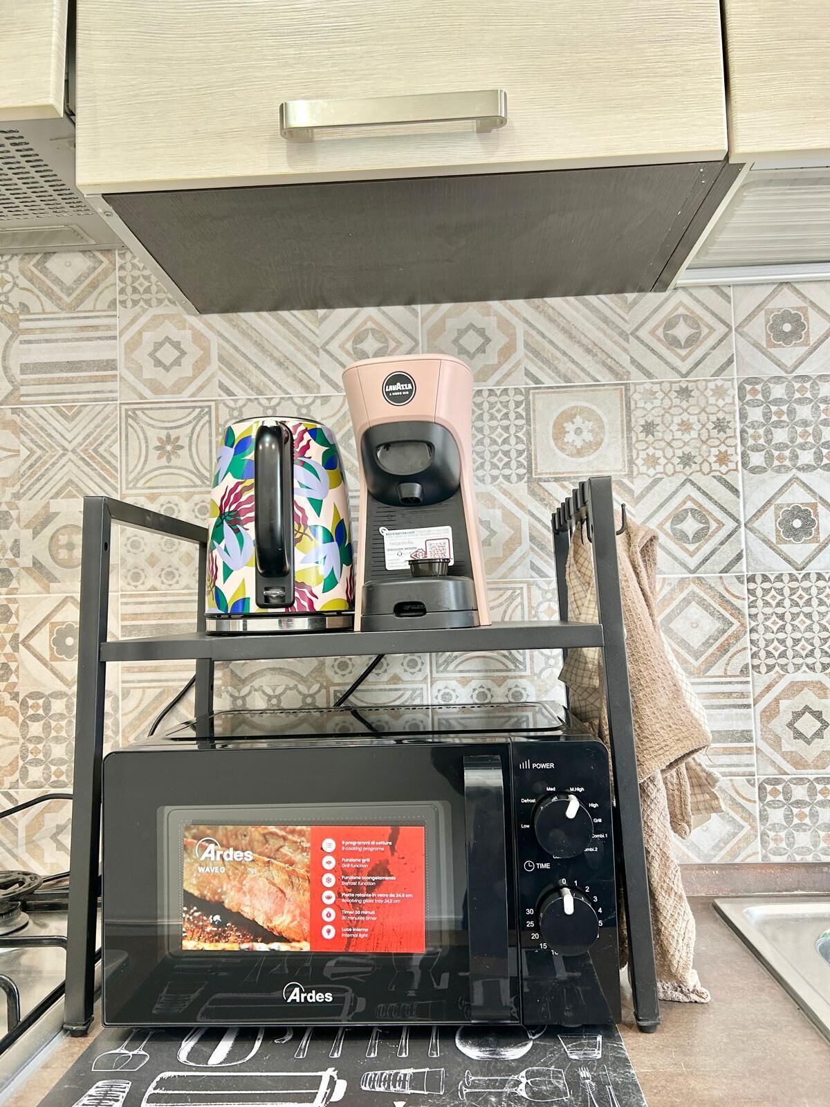 Una cocina con microondas, cafetera y un hervidor de colores en un estante.