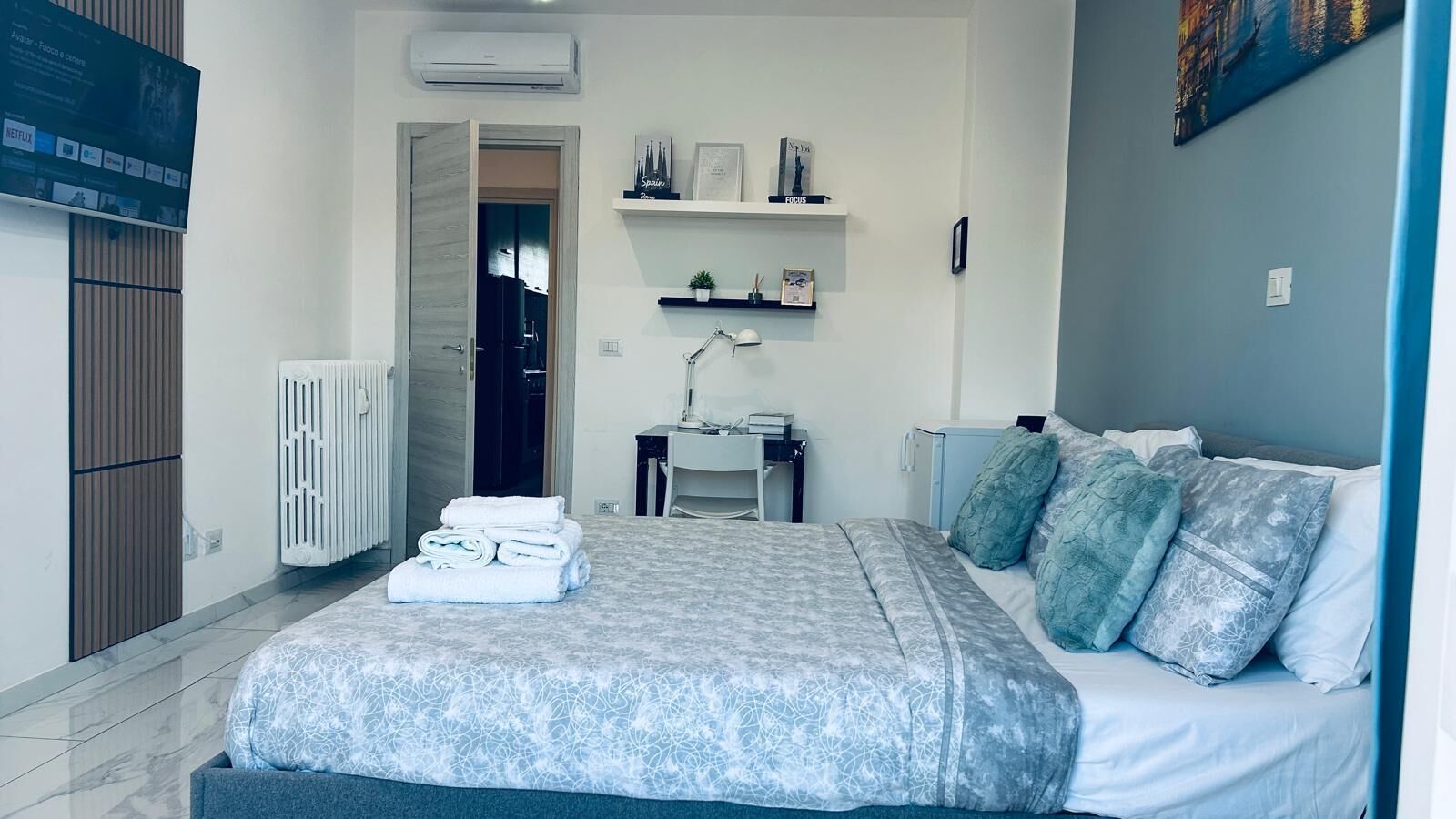 Une chambre à coucher comprenant un lit, un bureau, une chaise, un radiateur et un téléviseur fixé au mur.